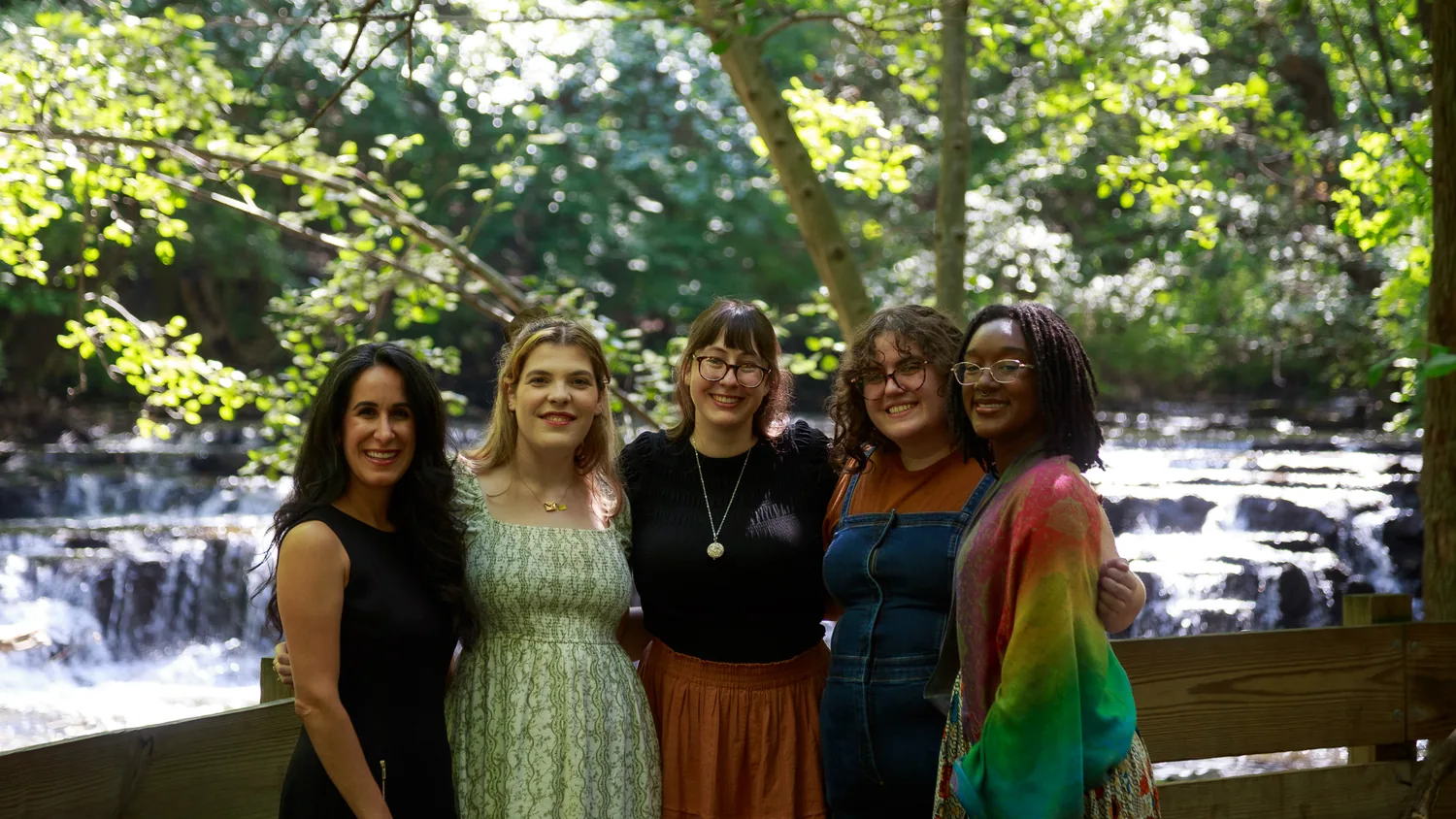 The five members of the Lumera Learning team standing arm in arm on a wooden bridge in front of a waterfall